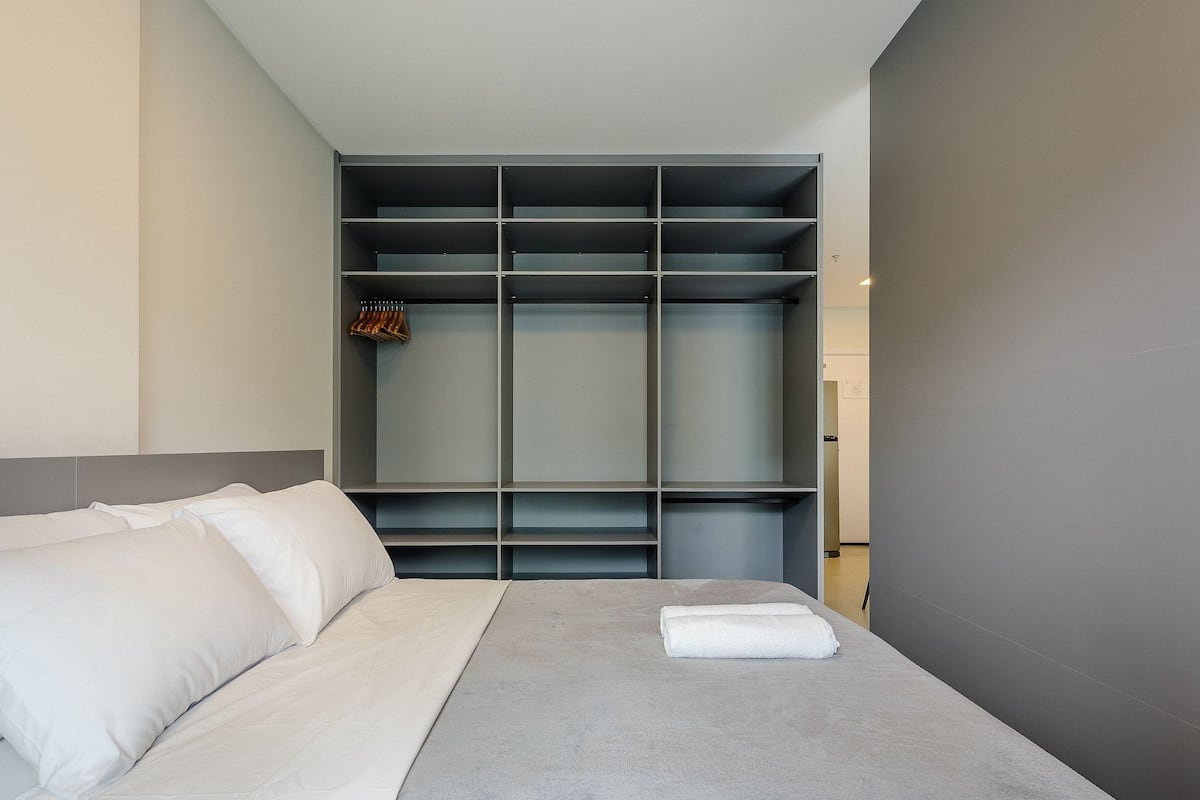 A modern hotel room with a bed, grey walls, and a built-in wardrobe with multiple shelves.