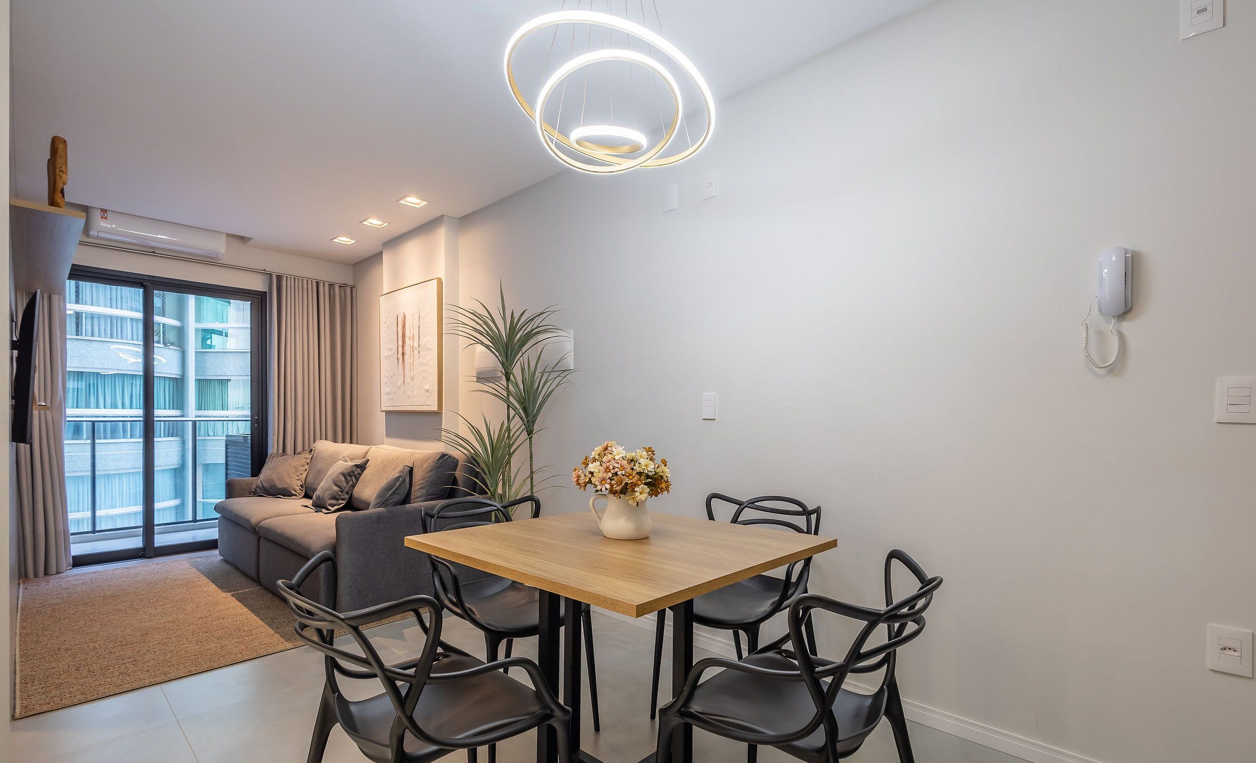 A modern living room with a sofa, a dining table with chairs, a potted plant, and a ceiling light fixture.