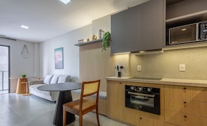 A modern kitchen with a built-in oven, a microwave, and a dining area with a round table and chairs. - Sua estadia exclusiva a poucos passos do Mar em Meia Praia - FFS (Itapema)