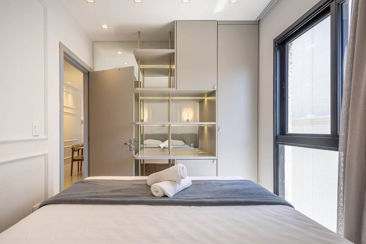 A modern hotel room with a bed, a built-in wardrobe, and a large window.
