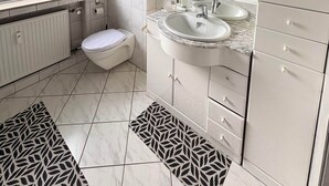 A bathroom with a toilet, sink, and mirror. There are shelves above the sink and a radiator below. - Charming Apartment in Quiet Ubbedissen (Bielefeld)