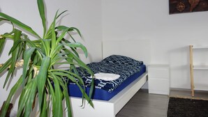 A single bed with a patterned bedspread, a large potted plant, and a wall-mounted world map. - Charming Apartment in Quiet Ubbedissen (Bielefeld)