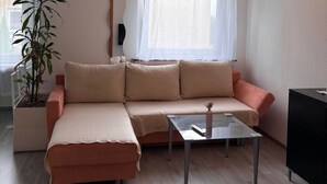 A living room with a beige sofa, a glass coffee table, a potted plant, and a window with sheer curtains. - Charming Apartment in Quiet Ubbedissen (Bielefeld)