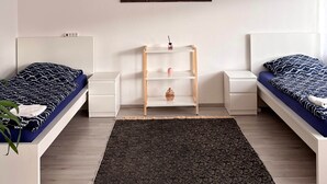 A minimalist bedroom with two single beds, a world map artwork, a small wooden shelf, and a dark patterned rug. - Charming Apartment in Quiet Ubbedissen (Bielefeld)