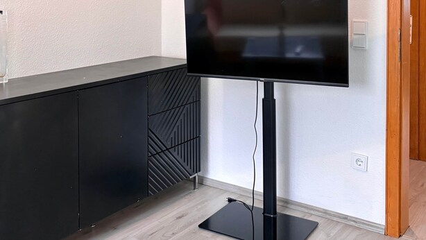 A flat-screen TV mounted on a wall, a black cabinet with geometric patterns, and a wooden door. - Charming Apartment in Quiet Ubbedissen (Bielefeld)