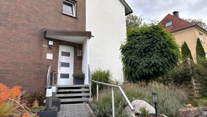 A two-story building with a brick facade, a white exterior wall, and a small front porch with steps leading to the door. - Charming Apartment in Quiet Ubbedissen (Bielefeld)