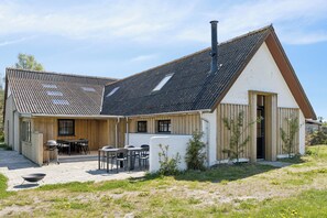 Ein Holzhaus mit geneigtem Dach, einer Terrasse mit Sitzgelegenheit und einem Schornstein.