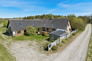Ein zweistöckiges Haus mit Kopfsteinpflasterauffahrt, einem umzäunten Garten und einem Wald im Hintergrund.