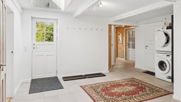 A laundry room with a washing machine, a door with a window, and a rug on the floor. - Holiday on lovely nature plot for families (Hadsund)