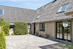 Een gebouw met een schuin dak, een geplaveid binnenhof en potplanten.
