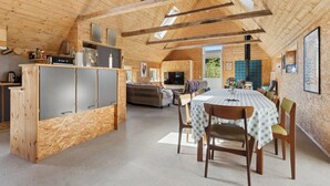 A spacious loft with a high ceiling, wooden beams, a kitchen area, a dining table, and a living area. - Holiday on lovely nature plot for families (Hadsund)