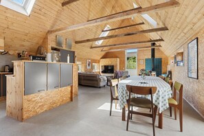 A spacious loft with a high ceiling, wooden beams, a kitchen area, a dining table, and a living area. - Holiday on lovely nature plot for families (Hadsund)