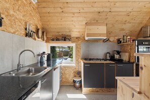 A modern kitchen with a wooden ceiling, built-in appliances, and a large window. - Holiday on lovely nature plot for families (Hadsund)