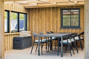 A wooden deck with a table and chairs, a bench, and a window.