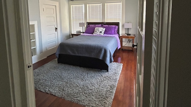 Un dormitorio con cama, ventilador de techo, ventana con persianas, mesita de noche y cómoda.
