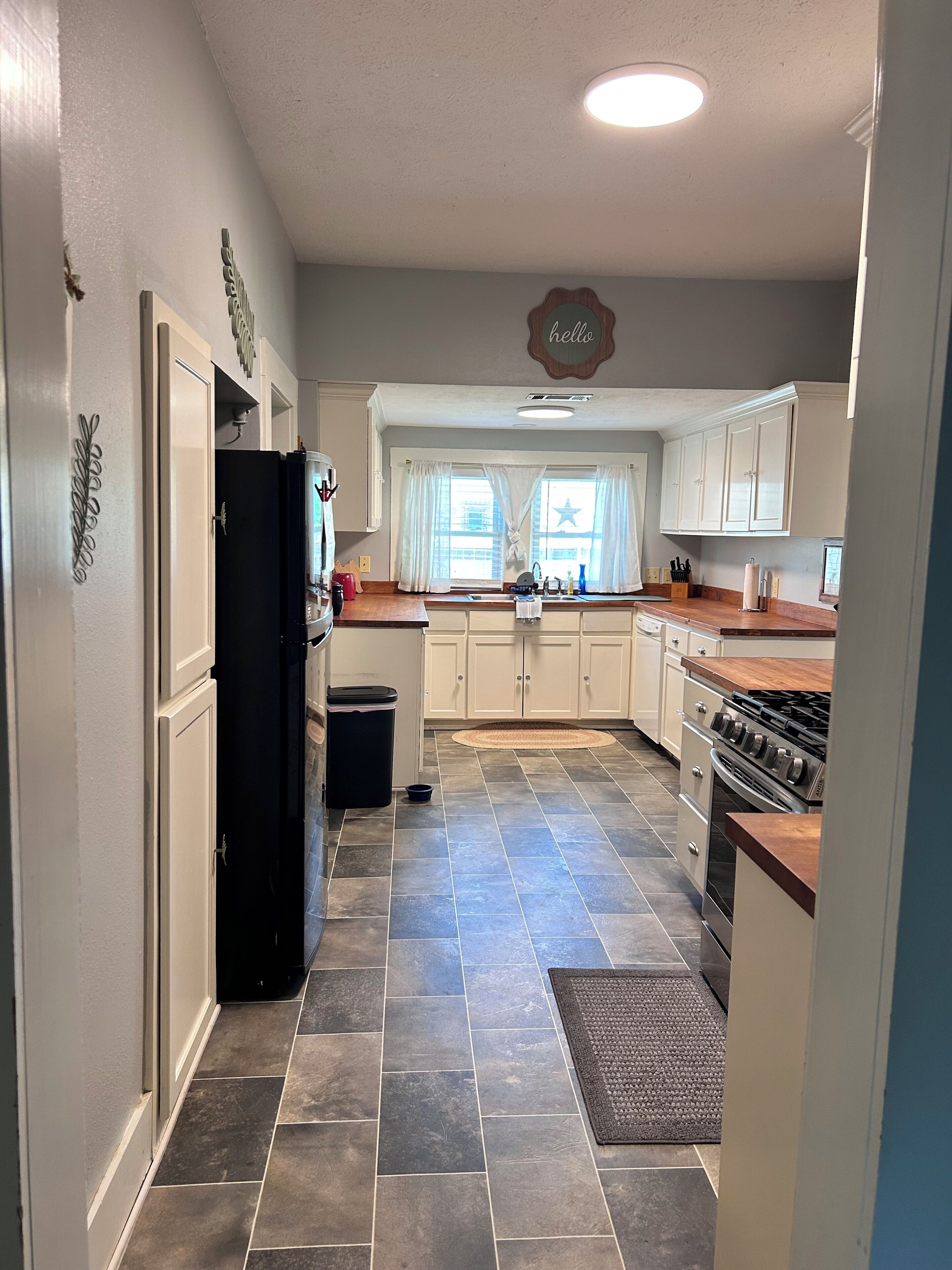 A kitchen with a black refrigerator, white cabinets, a stove, and a window with curtains.