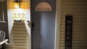 Una puerta principal con el número '135' arriba, un letrero de bienvenida y una silla a la izquierda.
