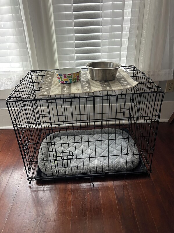 A pet cage with a bed and bowls on top.