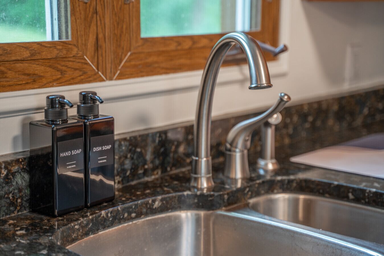 A kitchen sink with a modern faucet and two hand soap dispensers on a granite countertop.