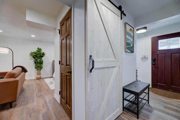 Un pasillo con puerta de madera, un banco, una planta en maceta y un sofá.