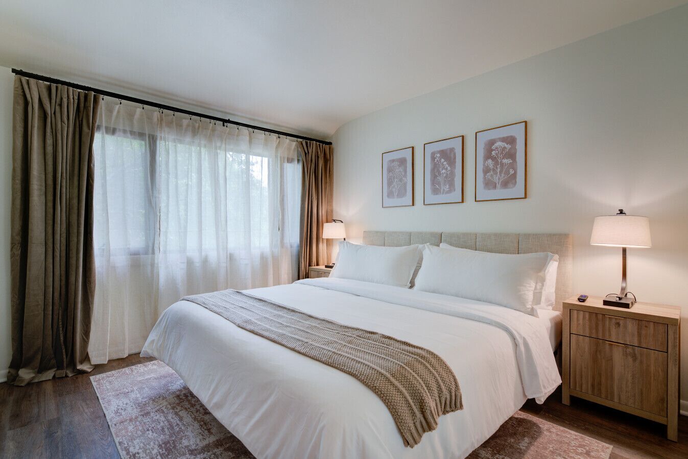 Ein Hotelzimmer mit einem großen Bett, zwei Nachttischen mit Lampen, einem Holzbeistelltisch und drei gerahmten Bildern an der Wand.