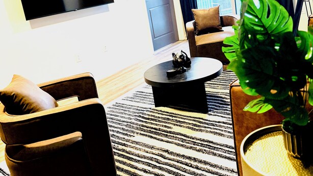 Una sala de estar moderna con un televisor de pantalla plana, un sofá, una mesa de centro y un ventanal con cortinas.