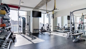 Un gimnasio moderno con diverso equipo de ejercicio, ventanas amplias y vistas a la ciudad.