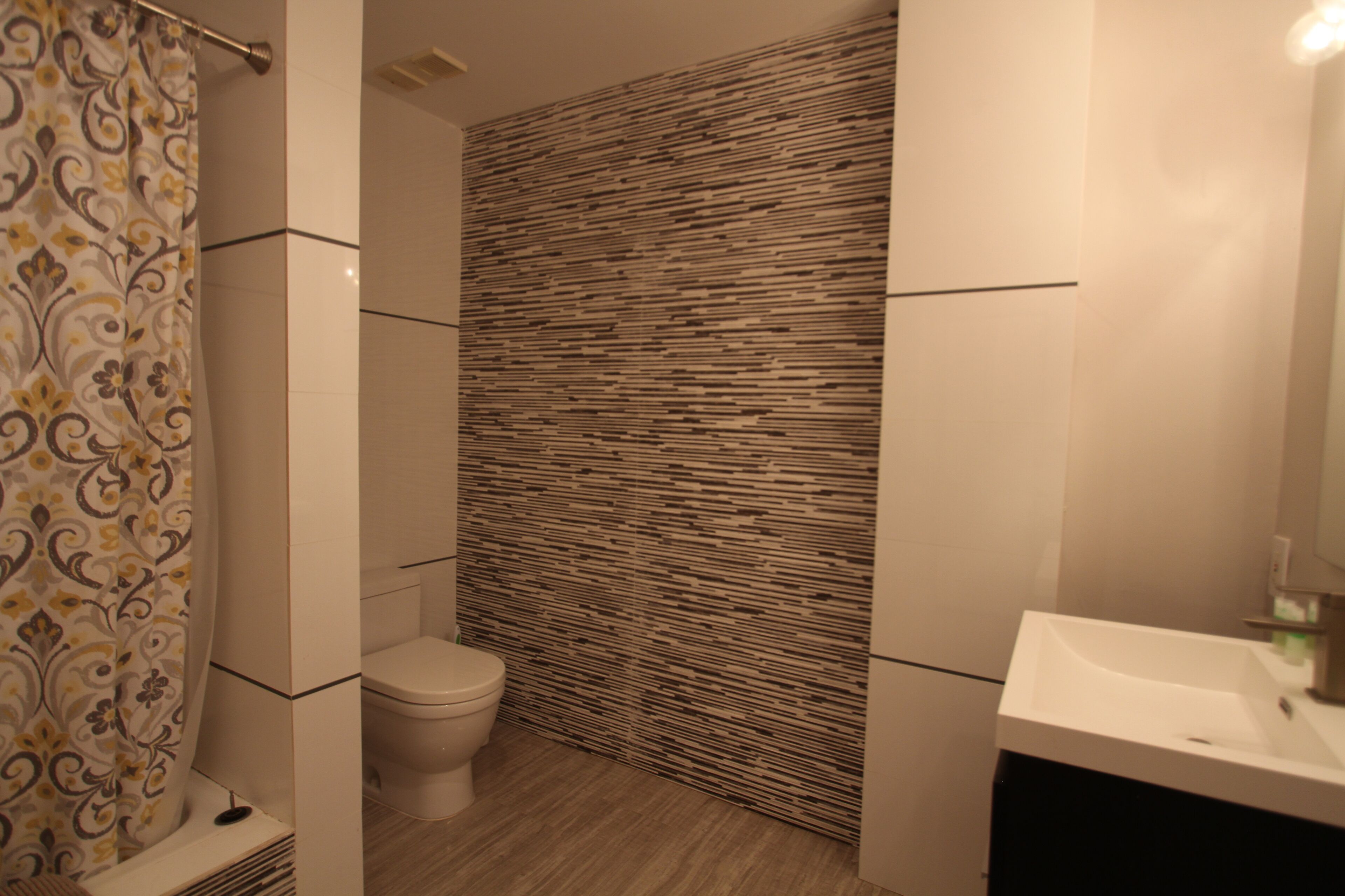 A bathroom with a patterned shower curtain, a toilet, a wall with a wood-like texture, and a white sink.