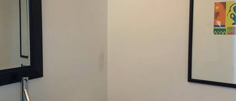 Une salle de bain avec un lavabo en verre, des toilettes blanches, un miroir à cadre noir et une œuvre d’art encadrée accrochée au mur.