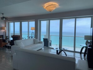 A spacious living room with a white sofa, a glass coffee table, and a view of the ocean through large windows. - Penthouse oceanview (Miami Beach)