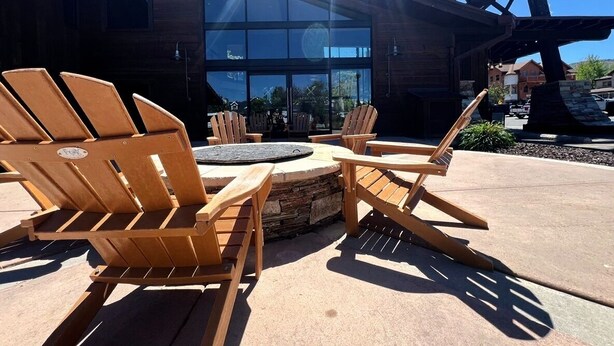 Espace extérieur aménagé avec des chaises Adirondack et un foyer en pierre, situé devant un bâtiment doté de grandes fenêtres.