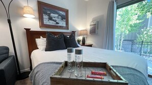 Une chambre d’hôtel avec un lit, des lampes de chevet, un tableau encadré au mur et une fenêtre donnant sur des arbres.