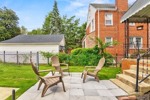 A patio with two Adirondack chairs, a brick house, and a white garage. - Chic DC Estate - Free Parking, Patio, Sleeps 8 (Washington)