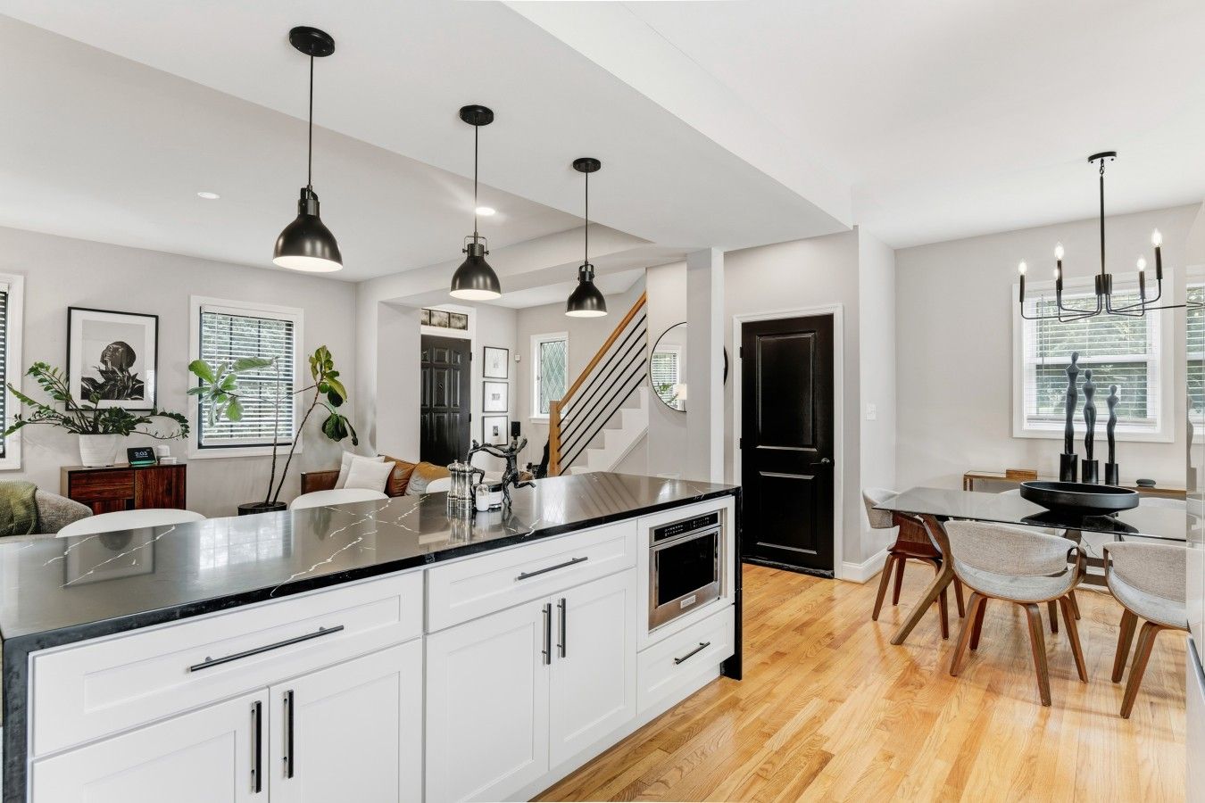 A modern kitchen with white cabinetry, a large island, pendant lighting, and a dining area with wooden chairs.