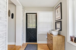 A hallway with a black door, a window with blinds, a wooden dresser, and a framed certificate on the wall. - Chic DC Estate - Free Parking, Patio, Sleeps 8 (Washington)