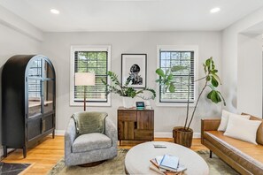 Una sala moderna con sofá, sillón, mesa de centro, estantería y plantas en macetas.