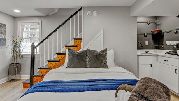 Een slaapkamer met een bed, een trap, een raam en een kitchenette.
