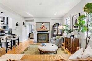 A modern living room with a fireplace, a dining area with bar stools, and a kitchen with a stove. - Chic DC Estate - Free Parking, Patio, Sleeps 8 (Washington)