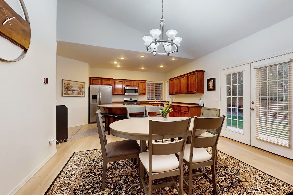 A modern kitchen with wooden cabinets, a central island, and a dining area with chairs and a table.