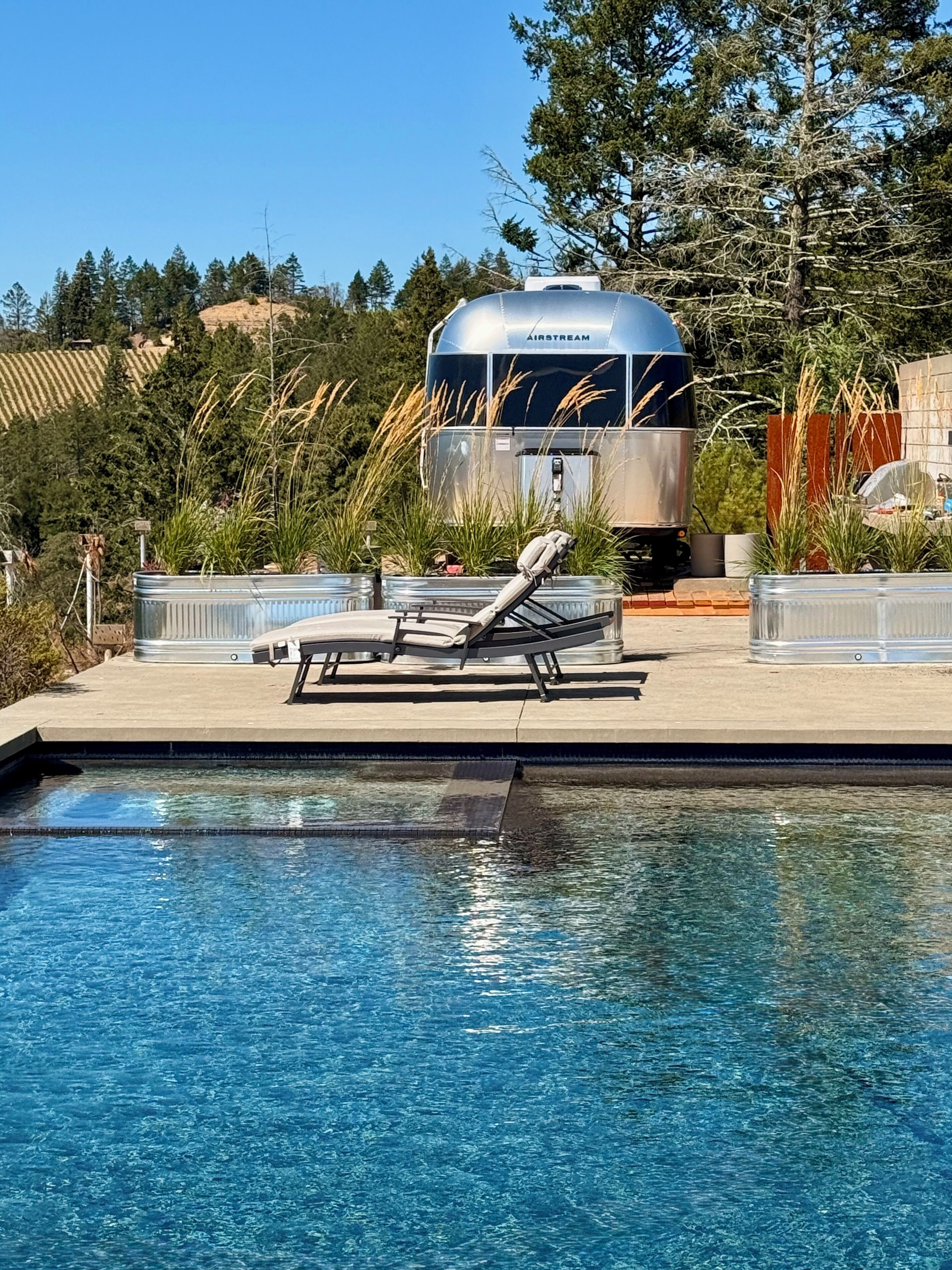 A swimming pool with lounge chairs and a covered RV named 'AIRSTREAM' in the background.