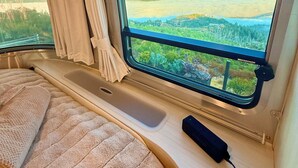 A cozy interior with a bed, a window with curtains, and a view of a landscape.