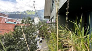 Une vue d’un bâtiment doté d’un balcon, entouré de verdure, avec un paysage montagneux en arrière-plan.