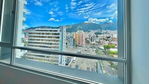 A view from a window overlooking a cityscape with buildings and mountains. - Luxury 2BR + Gym & City Views| Near Spain Embassy (QUITO)