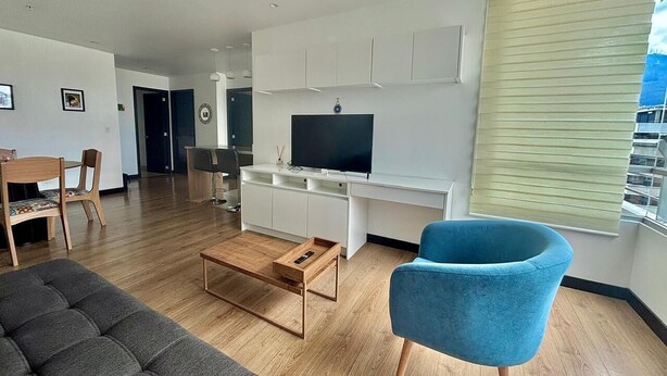 A modern living room with a sofa, a blue armchair, a wooden coffee table, a TV, and a desk with cabinets. - Luxury 2BR + Gym & City Views| Near Spain Embassy (QUITO)