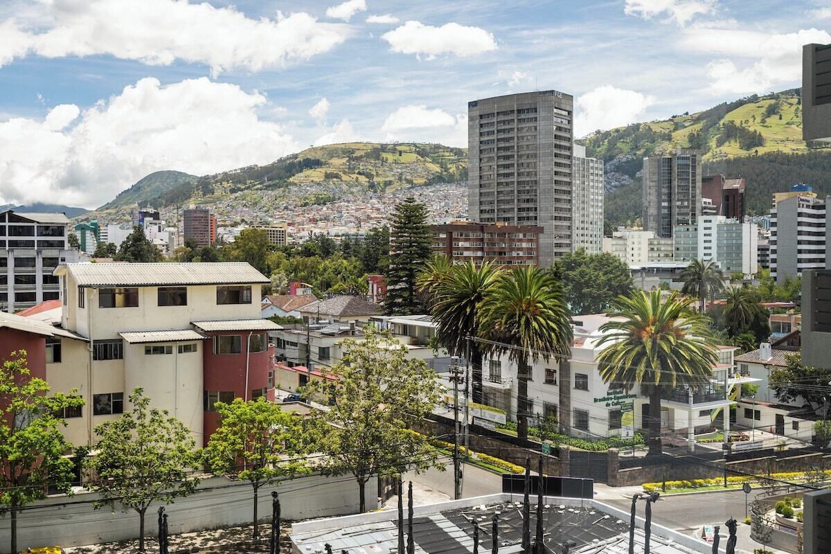 Un paysage urbain avec des bâtiments modernes, un gratte-ciel imposant et un arrière-plan vallonné.