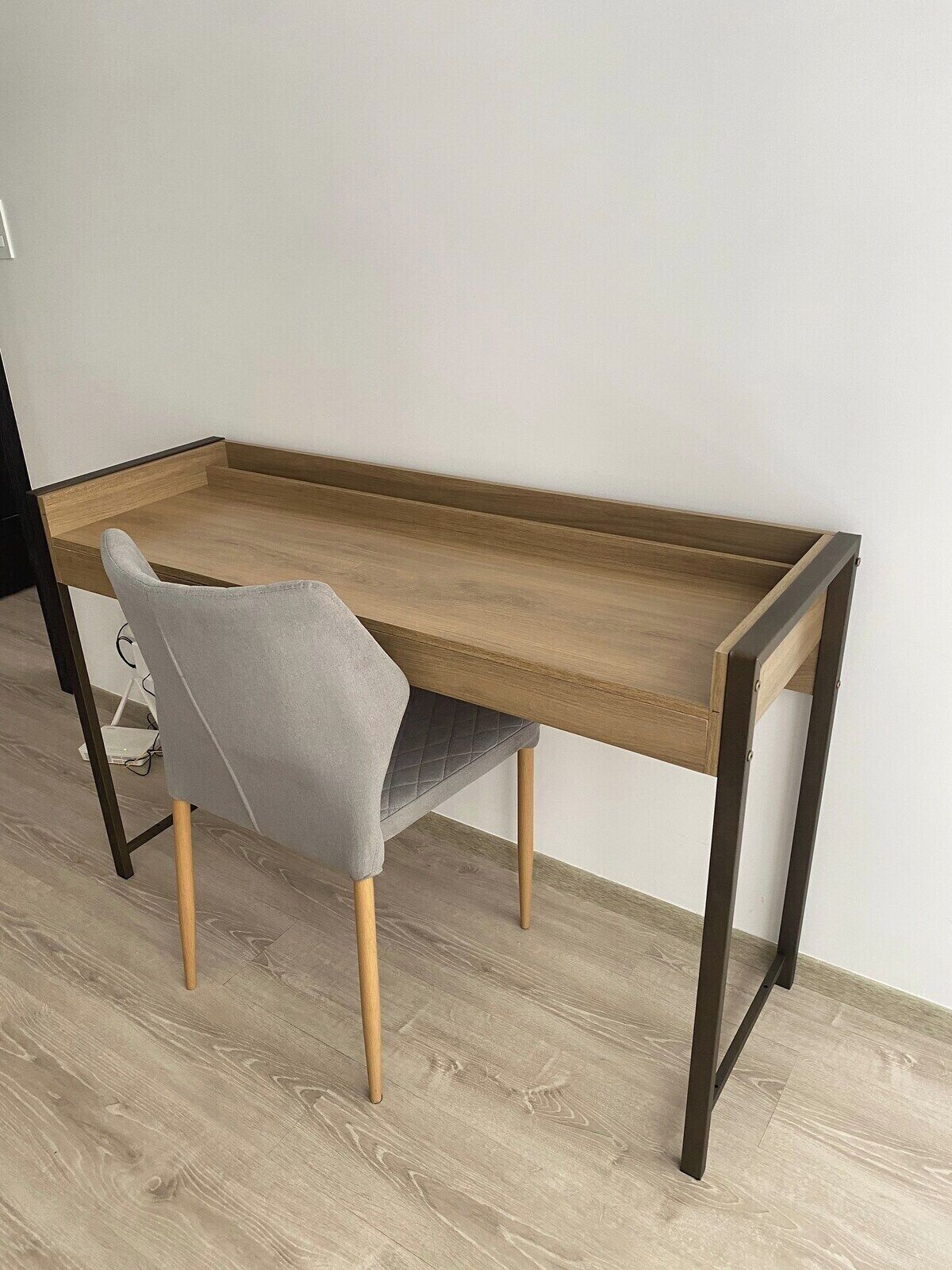 Et minimalistisk skrivebord med en grå polstret stol, træben og metalstel.
