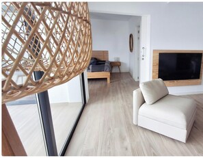 Een moderne woonkamer met een bank, een aan de muur bevestigde televisie en een rieten lamp.
