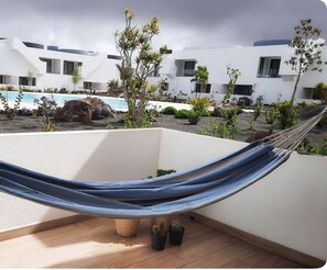 Una hamaca en un balcón con una piscina y edificios modernos al fondo.