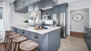 Une cuisine moderne avec des meubles gris, un îlot central blanc, des appareils en acier inoxydable et des tabourets en bois.