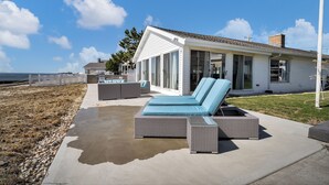 Un espace de détente extérieur moderne, avec un sol en béton, un grand canapé en osier doté de coussins bleus, et un bâtiment blanc en arrière-plan.
